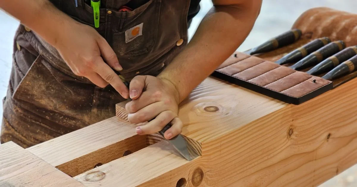 Close-up of hands carving joinery into a timber beam